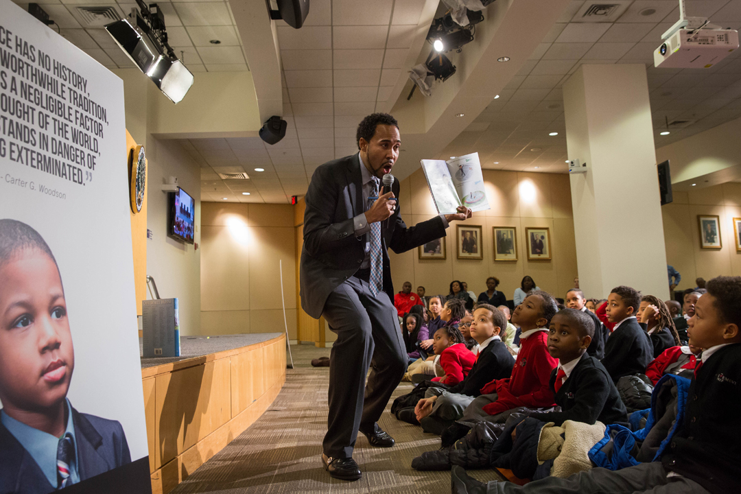 Person holding a mic talking to kids holding a book
