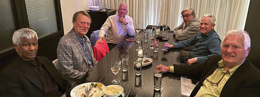 Six people are sitting around a dinner table posing for a photo