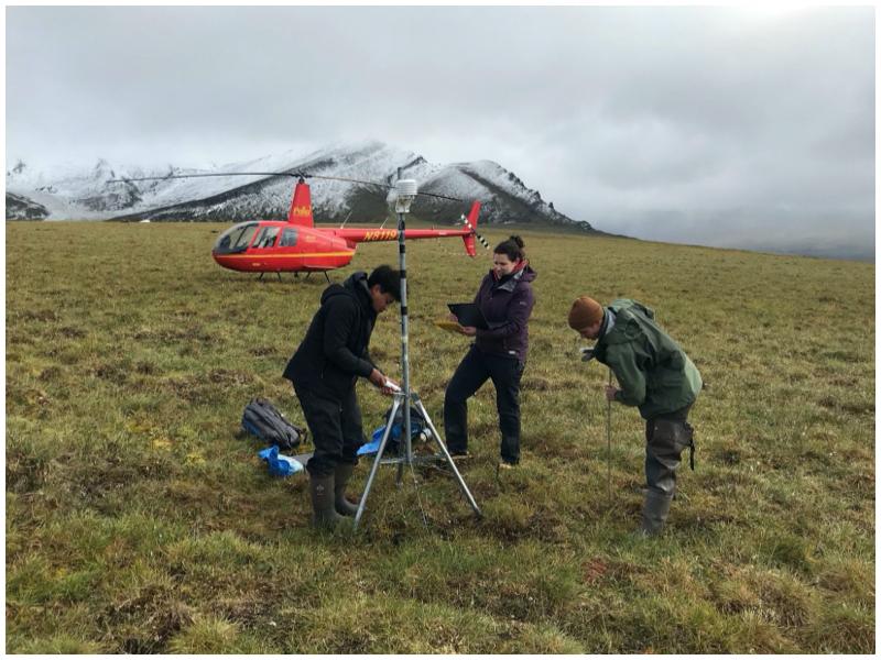 Students measuring permafrost thaw, a helicopter is in the background