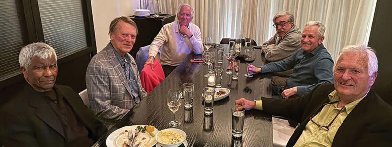 Six people are sitting around a dinner table posing for a photo